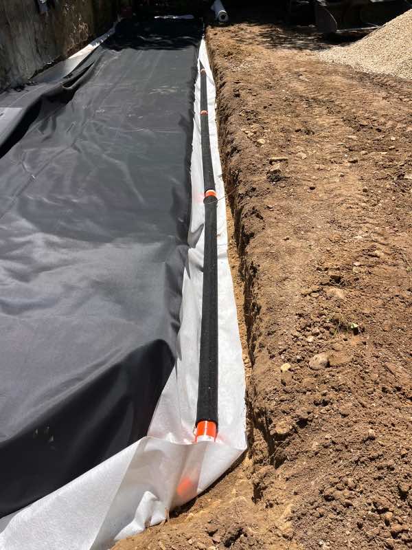 Drain enrobé avec raccords orange posé sur géotextile au fond de la tranchée