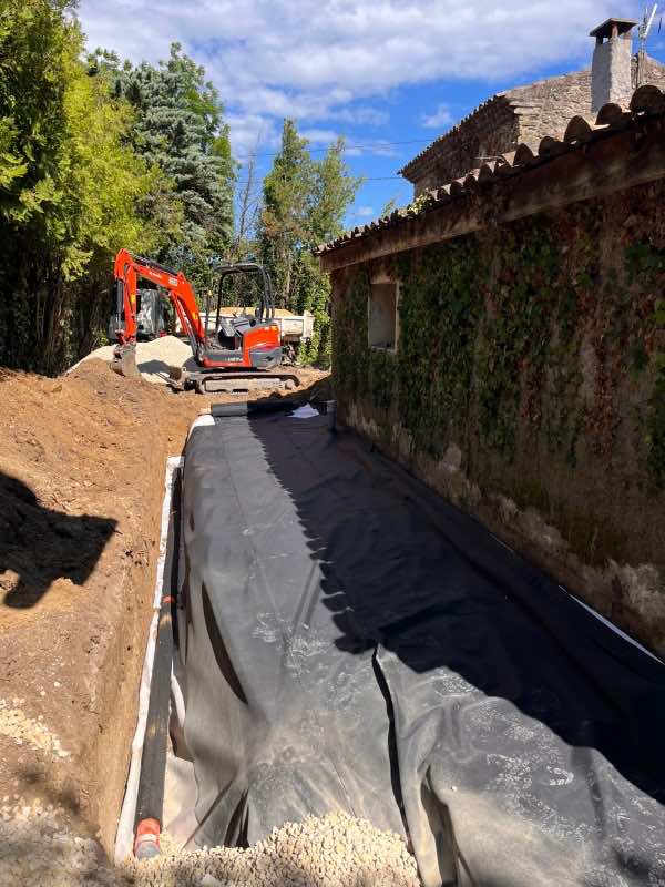 Tranchée de drainage le long d'une maison en pierre à Charols, mini-pelle en fond