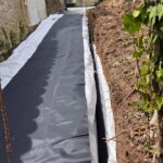 Drain noir enrobé posé en bord de géomembrane le long d'un mur en pierre