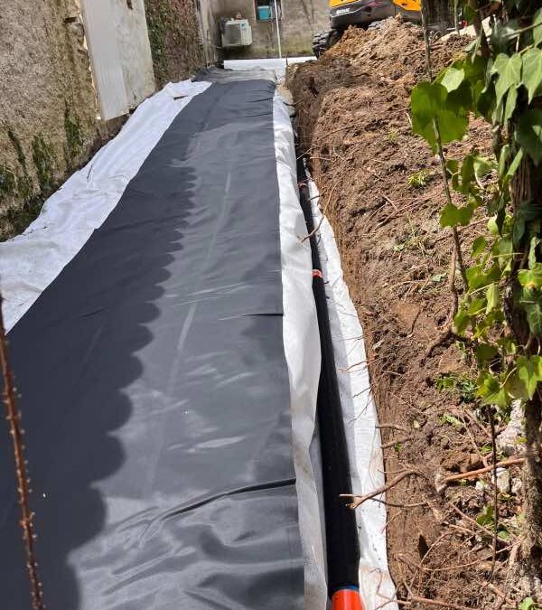 Drain noir enrobé posé en bord de géomembrane le long d'un mur en pierre